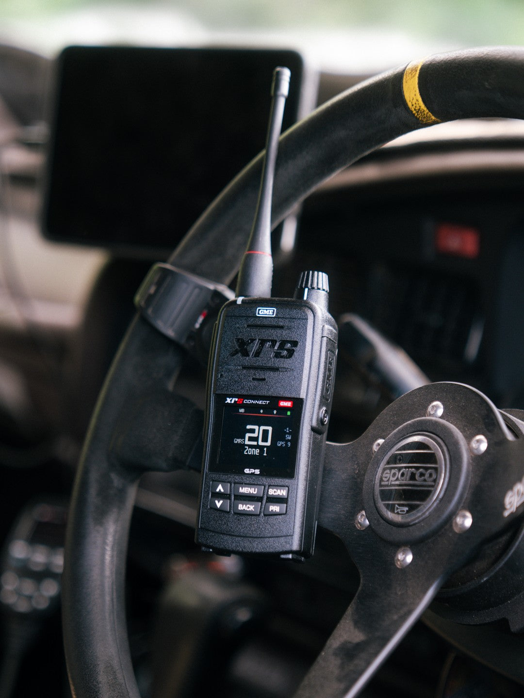 GME XRS-660-U handheld radio in front of a suede Sparco steering wheel, its screen showing GMRS channel 20 and GPS