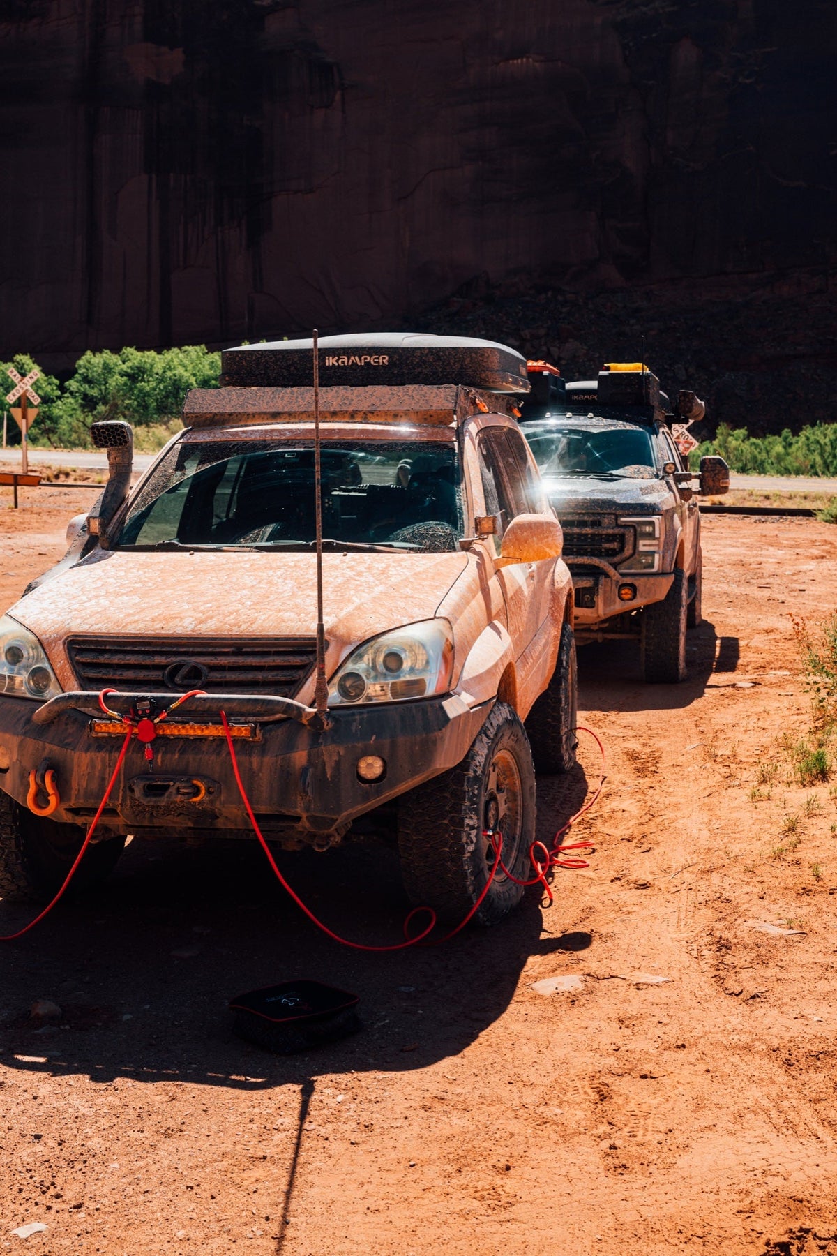 Tan SUV on a red dirt desert trail with its red synthetic winch rope run out ahead of it, a second rig behind