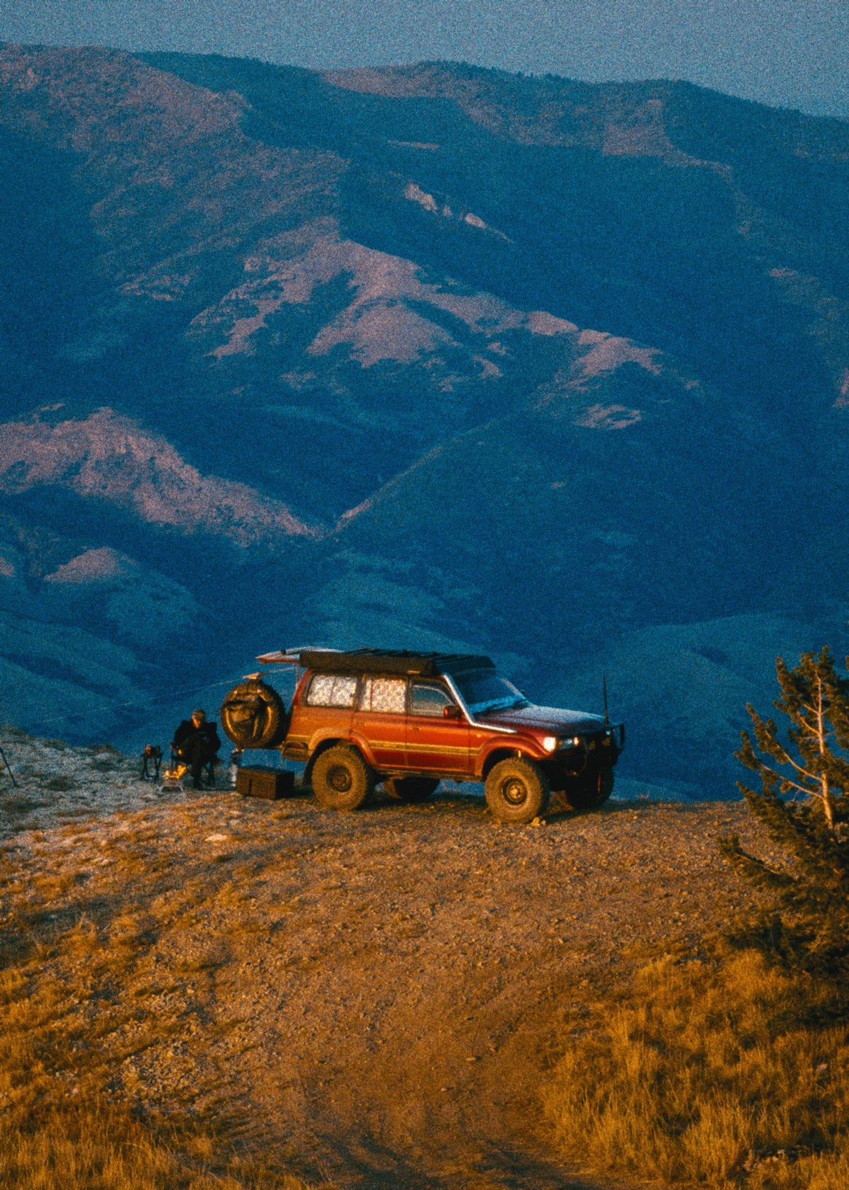 Red 80 Series Land Cruiser on a golden ridge point with blue mountains behind