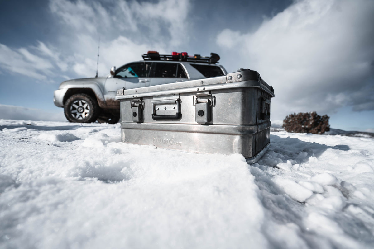 AluBox 42L aluminum case sitting in snow, latches and handle in view, a truck behind