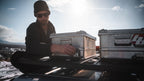 AluBox 42L aluminum case, a person securing a case on a vehicle roof rack, second case beside it
