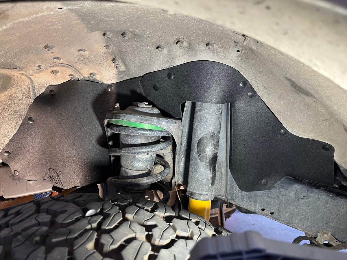 Ark rubber splash guard fitted in a Land Cruiser FZJ80 front wheel well, behind the coil spring and shock