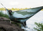 Someone stretched out in the Roo Double Printed hammock above the water's edge, Waves print in green and white