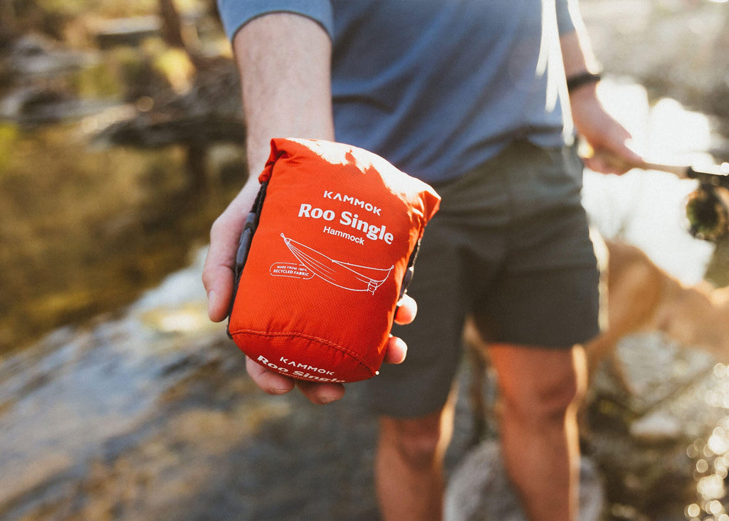 The Roo Single packed in its orange stuff sack, held in one hand beside a creek