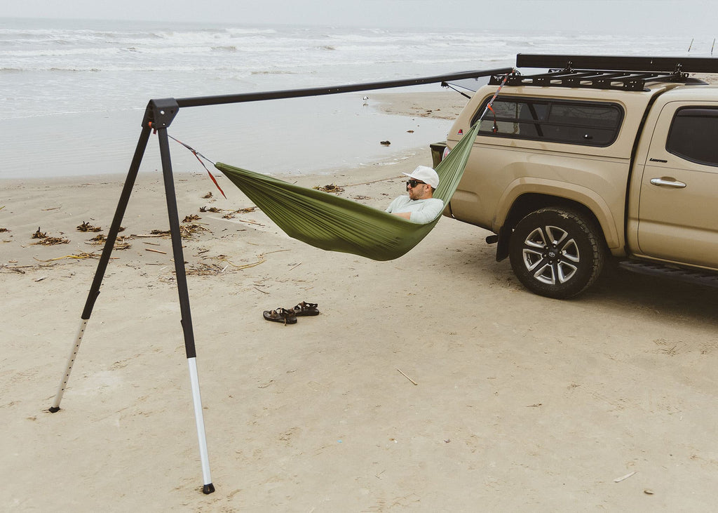 The Outpost standing free of trees on a beach, a green hammock hung from it next to a tan truck