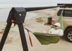 Close on the Outpost frame on a beach, someone resting in a green hammock beside a tan truck