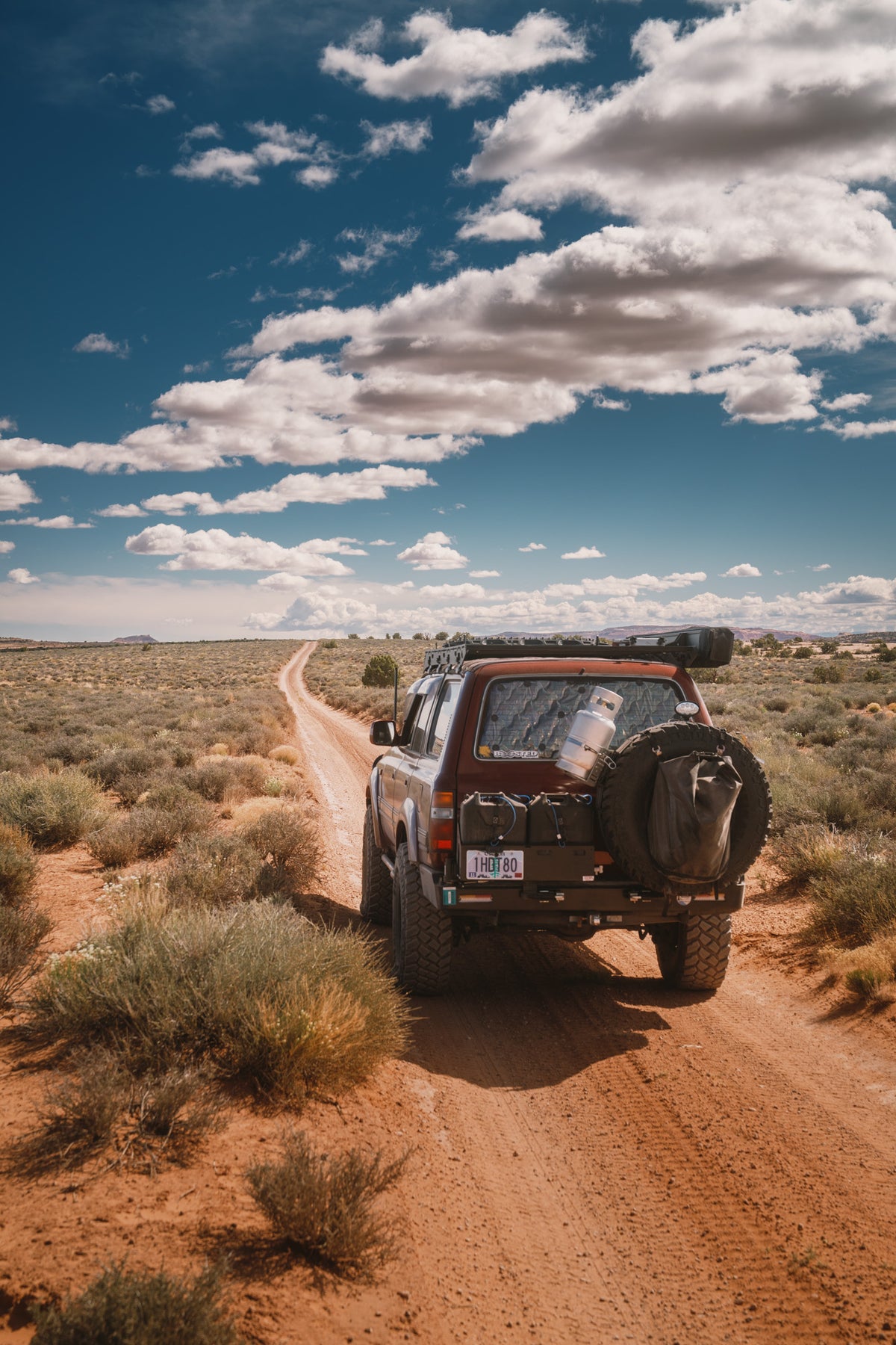 Our 80 Series from behind on a sandy desert two-track under big clouds, the Colfax Q.D. Tire Bag on the spare
