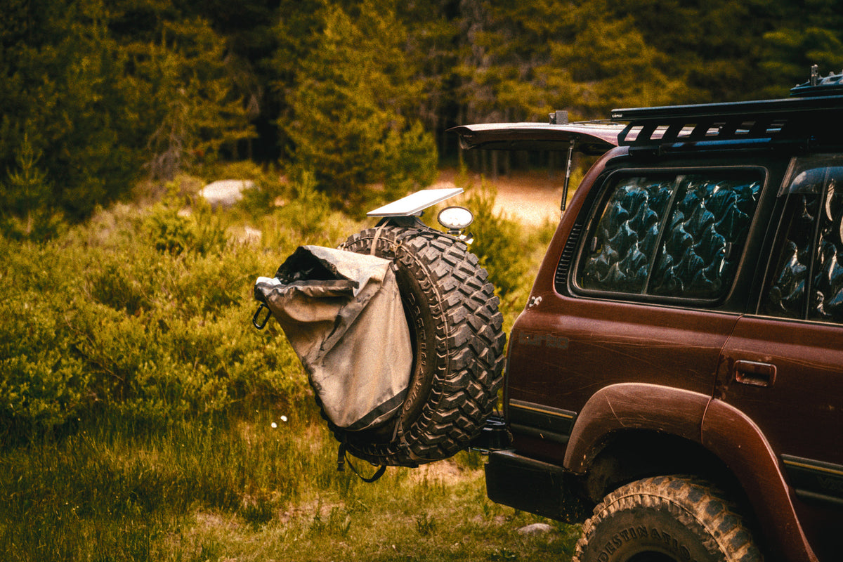 The Colfax Q.D. Tire Bag strapped to the spare on our 80 Series, parked in tall summer grass