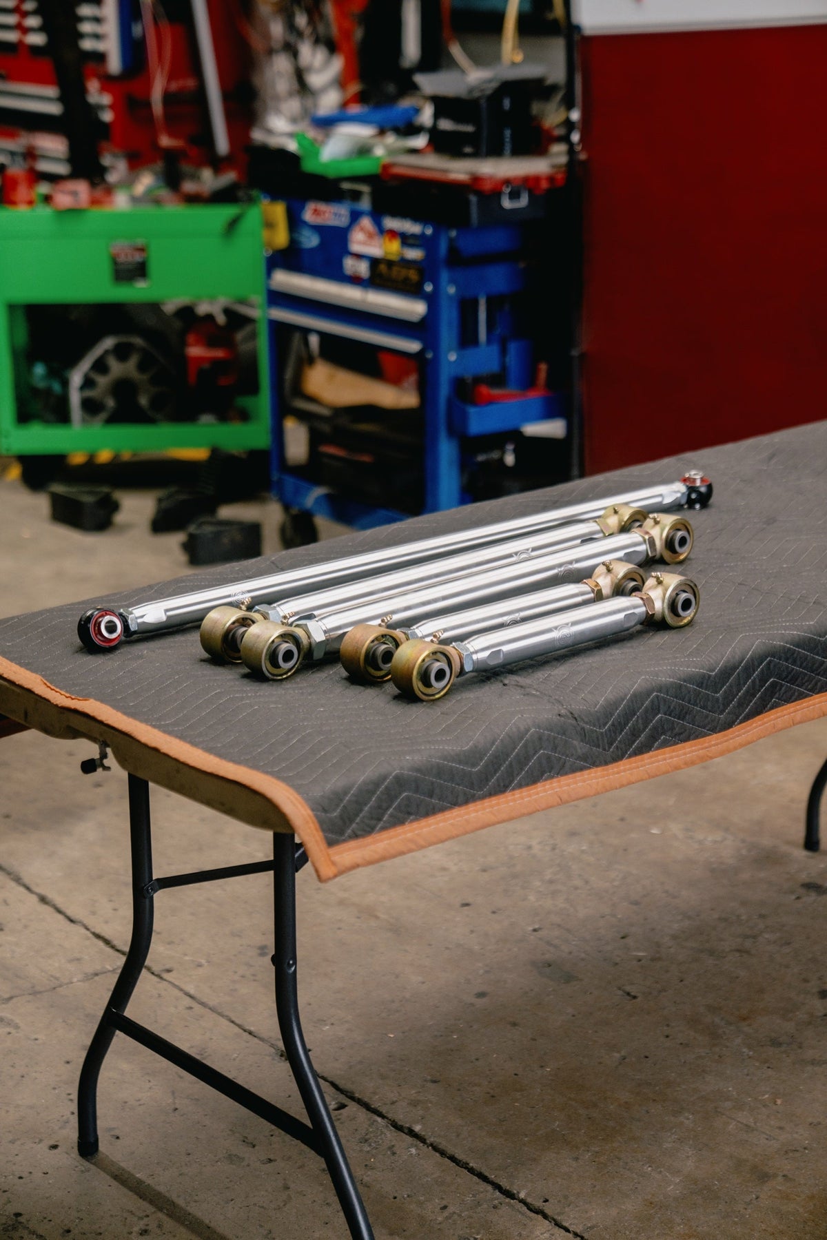 A set of Overland Custom Design upper and lower control arms laid out on a shop table before going on our 80 Series