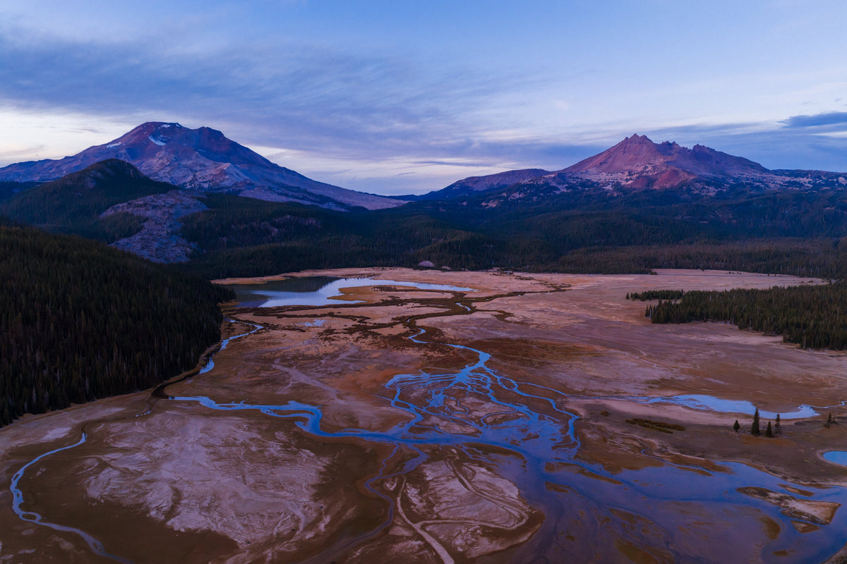 Braided streams across a meadow below two volcanic peaks at blue hour