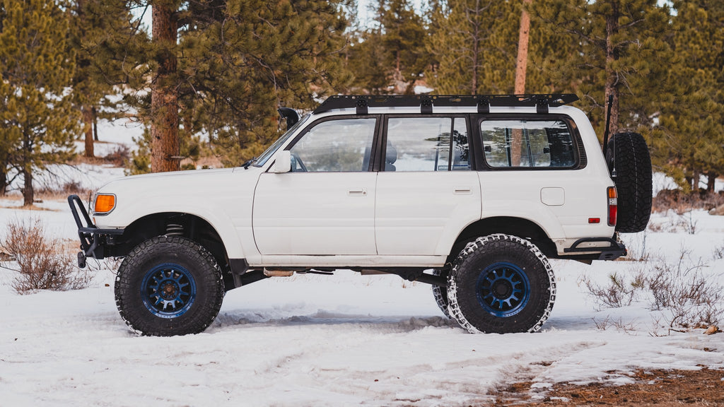 White 80 Series Land Cruiser side-on in snowy pines with a Sherpa La Sal rack