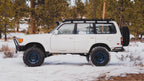 White 80 Series Land Cruiser side-on in snowy pines with a Sherpa La Sal rack