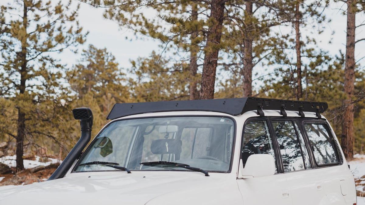 White 80 Series with snorkel and La Sal rack among pines in light snow